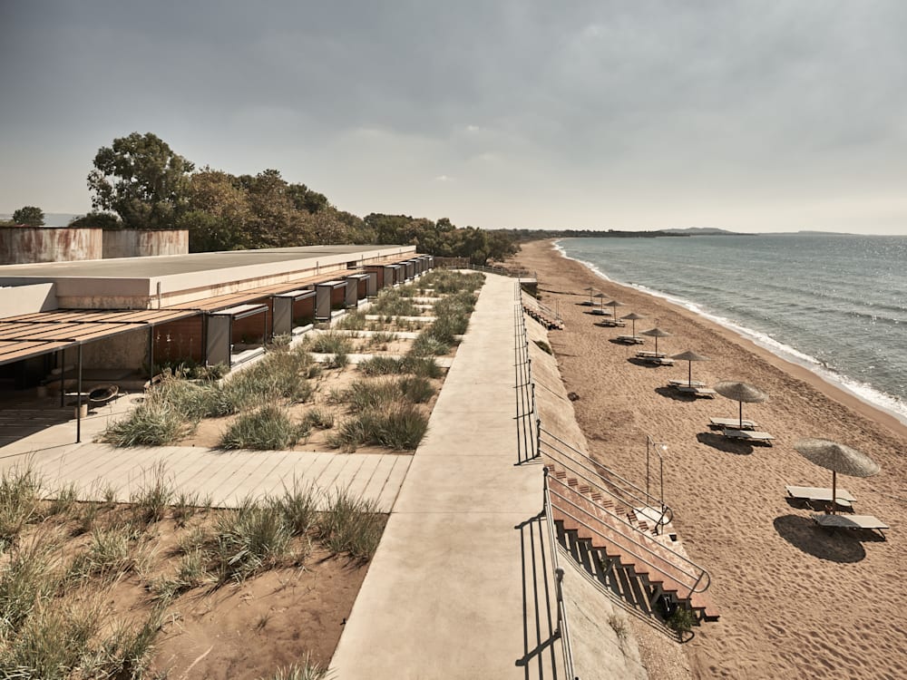 Eksterior hotel menghadap pantai berpasir dengan kursi berjemur dan payung 