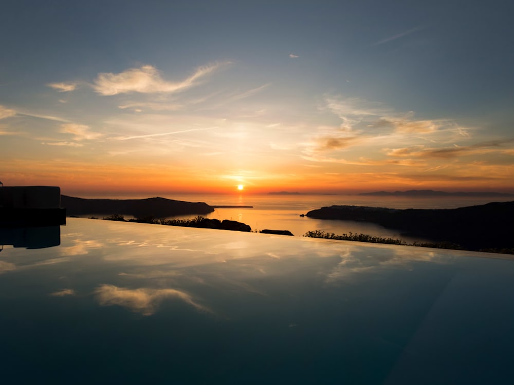 Deep orange sunset over the sea. The scattered clouds are reflected in the crystal clear still waters of the mirror-like infinity pool