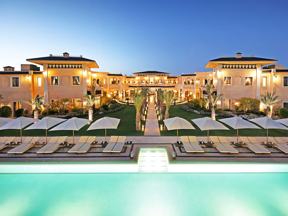 Swimming pool and hotel in the dusk, the hotel is lit up with a beautiful orange glow looking down onto the aquamarine swimming pool and sun beds