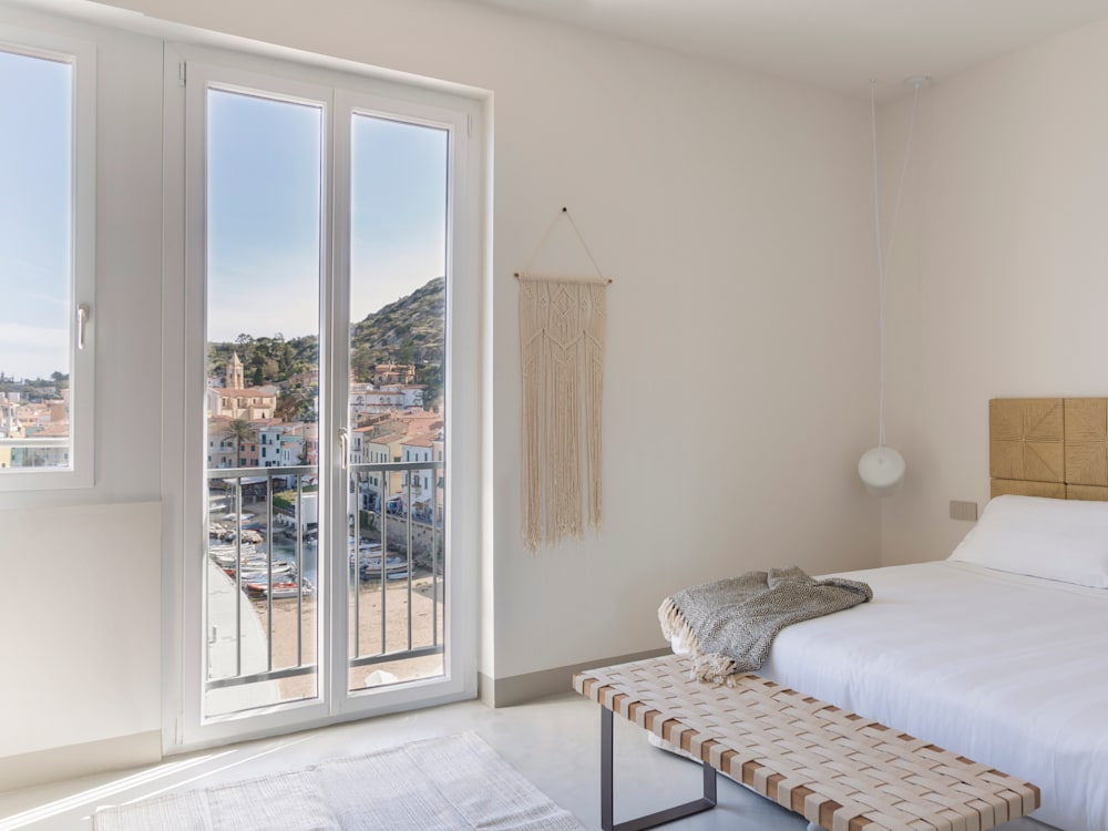 White washed bedroom and bed with views on to the beach and multicoloured houses on the Cliffside opposite