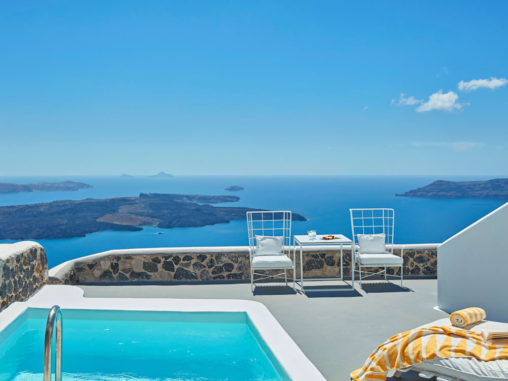 Master Suite terrace overlooking the ocean. The aquamarine private pool is crystal clear, a yellow striped beach towel is on the sun lounger. A table and two chairs are by the low wall. 