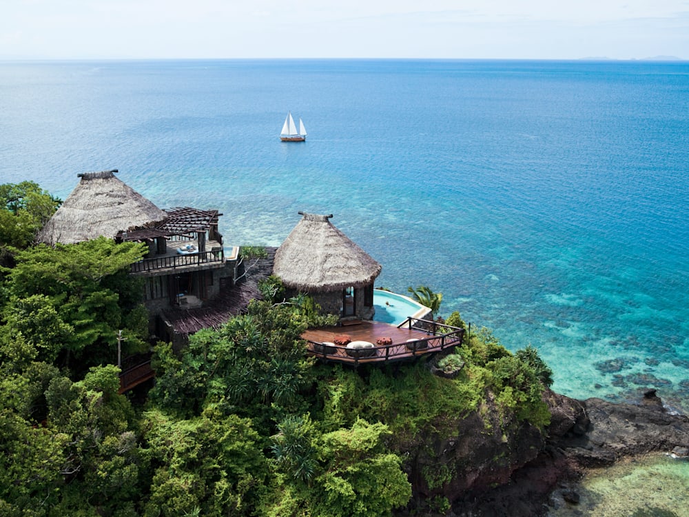 Residence nestled into the hillside surrounded by flora. The infinity pool looks out onto the ocean with a sailing boat in the distance. 
