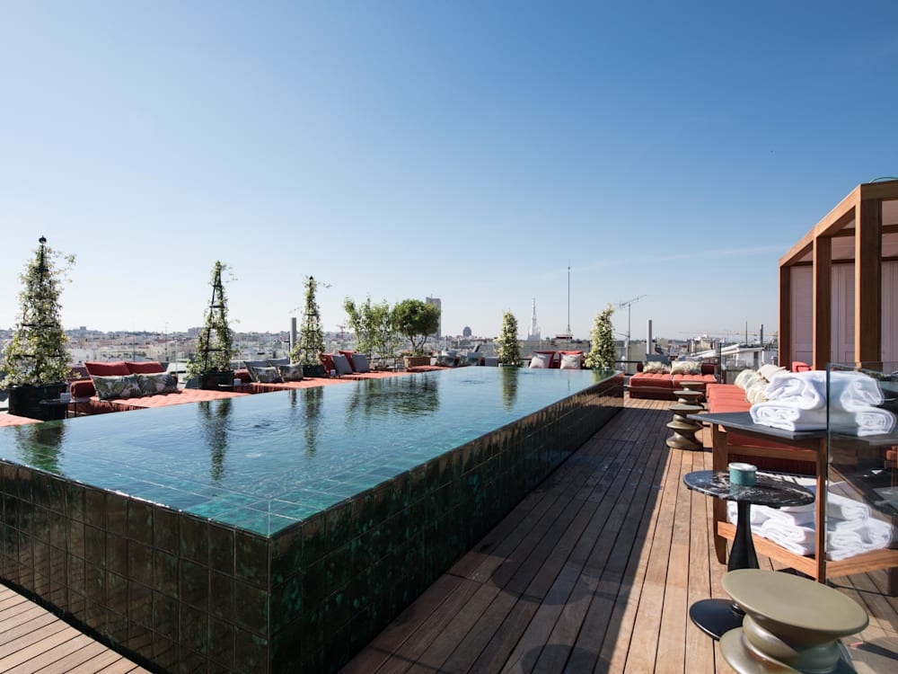 Swimming pool with glass mirror like water on the sun drenched roof terrace. There are 360 degree views of the city with sun loungers and cabanas surrounding the pool 