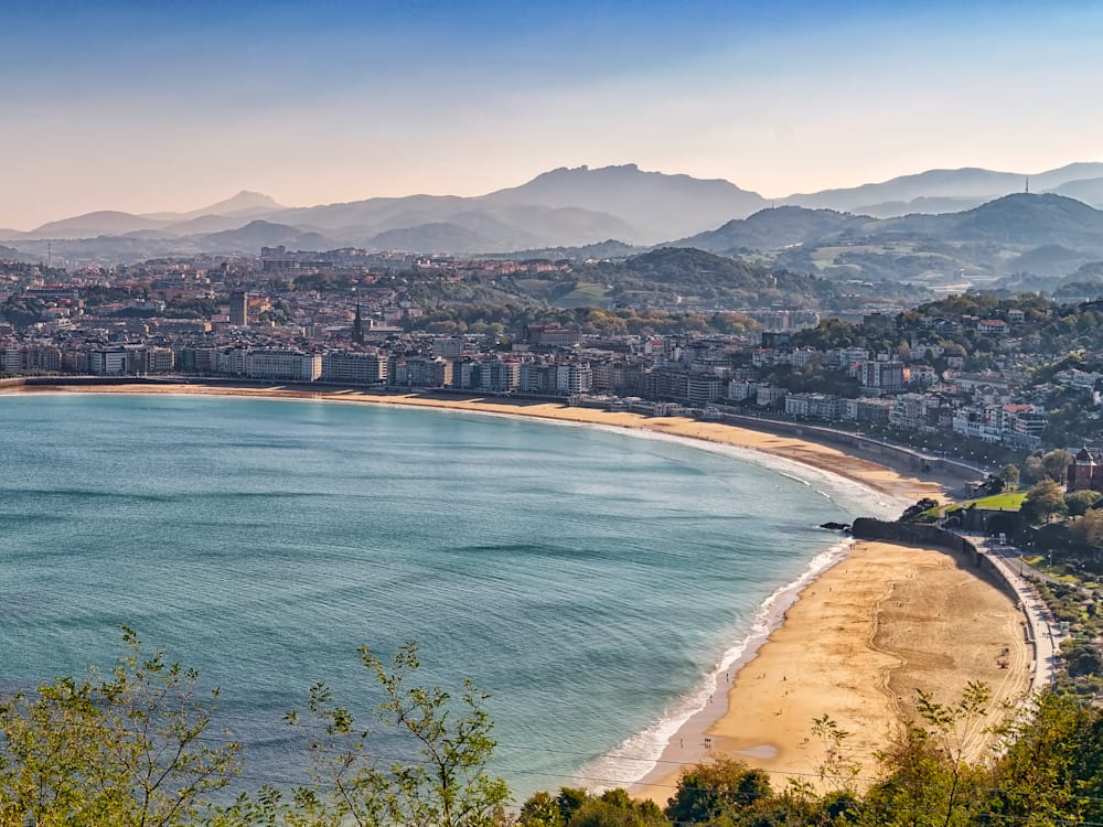 San Sebastián from across the bay. The mountains are hazy in the background and the sandy beaches are in the foreground. 
