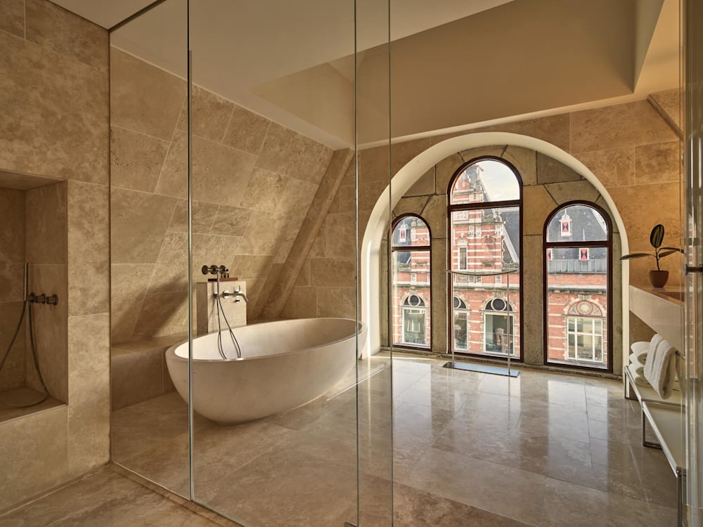 Stand alone bath in a glass walled bathroom. The arched windows look out onto the city. 