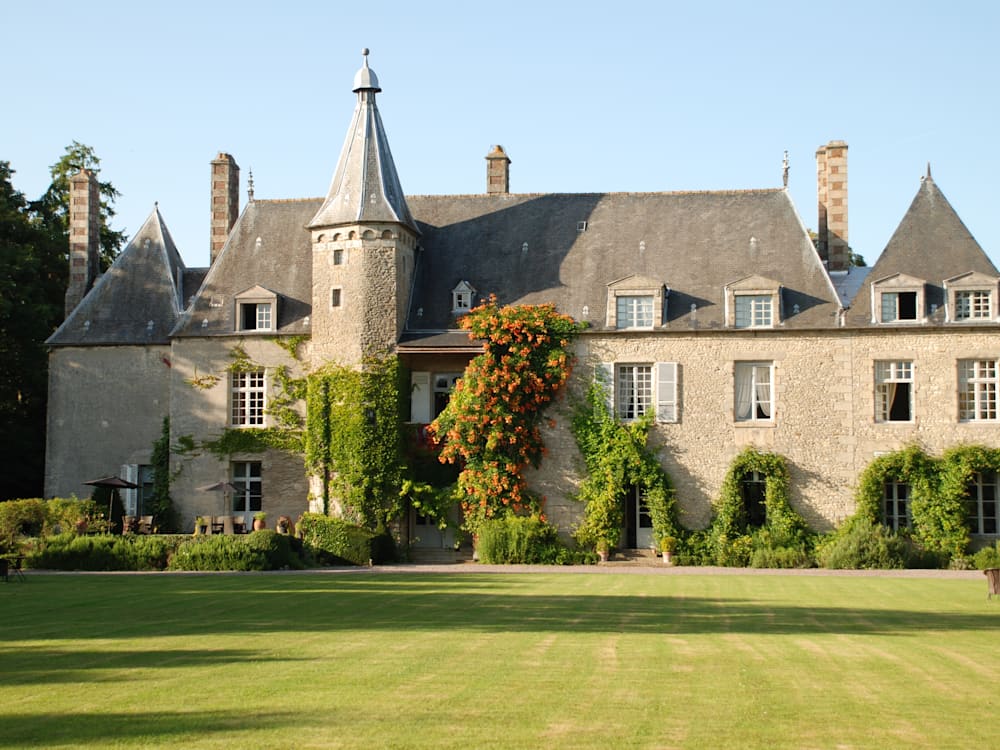 View of the chateau from the gardens. Ivy is climbing up the walls of the old building, it's turrets reaching up to the clear blue sky. 