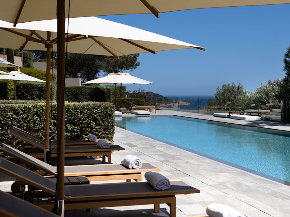 Sun loungers round the swimming pool with the hint of the deep blue sea in the background