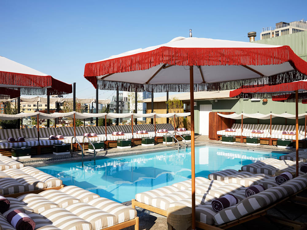 Rooftop swimming pool surrounded by striped sun loungers and parasols in the bright sunlight