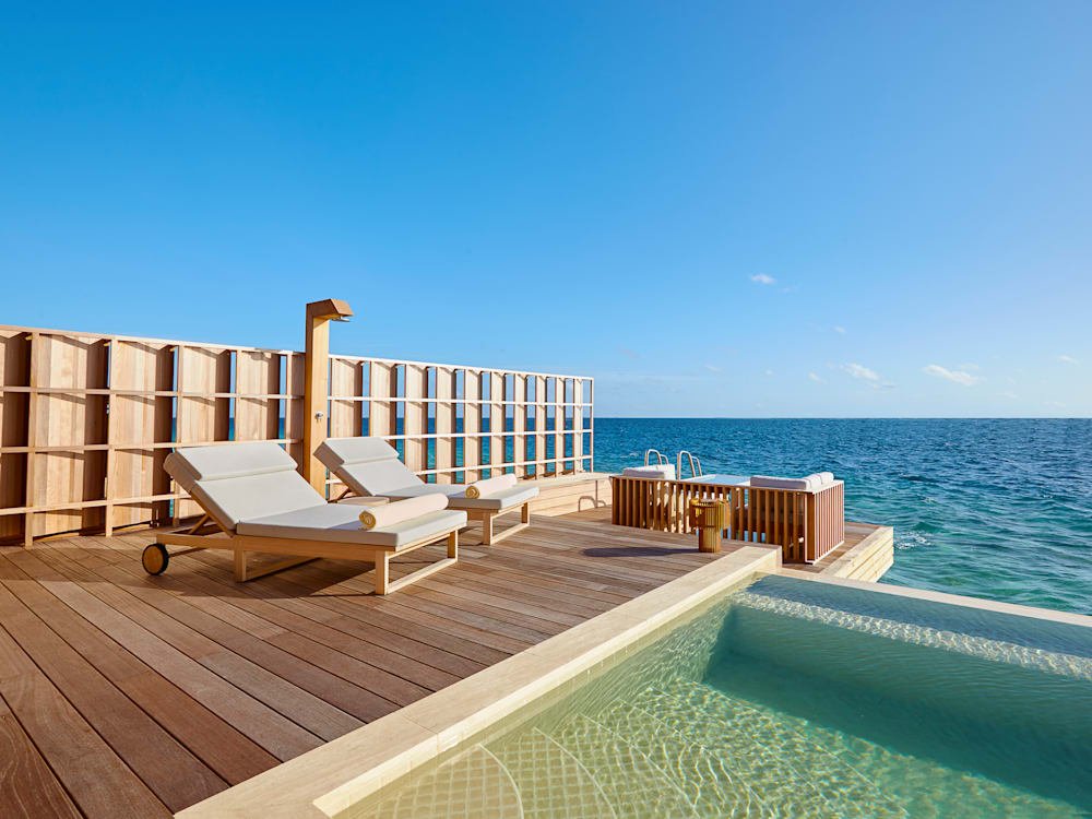 Sun loungers and infinity pool on a wooden deck looking at to the deep blue sea