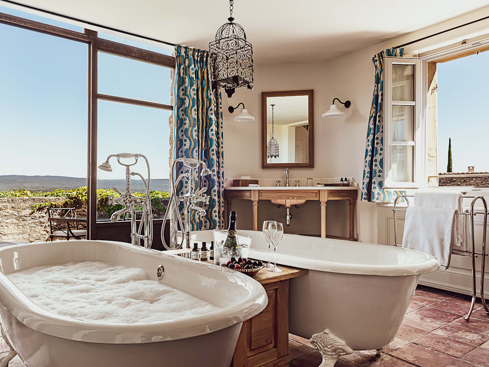 Double bathtubs filled to the brim with bubbles. Champagne and two glasses sit on the table in-between the baths. Sunlight is streaming in from the floor to ceiling windows looking out onto the plains of Provence. 