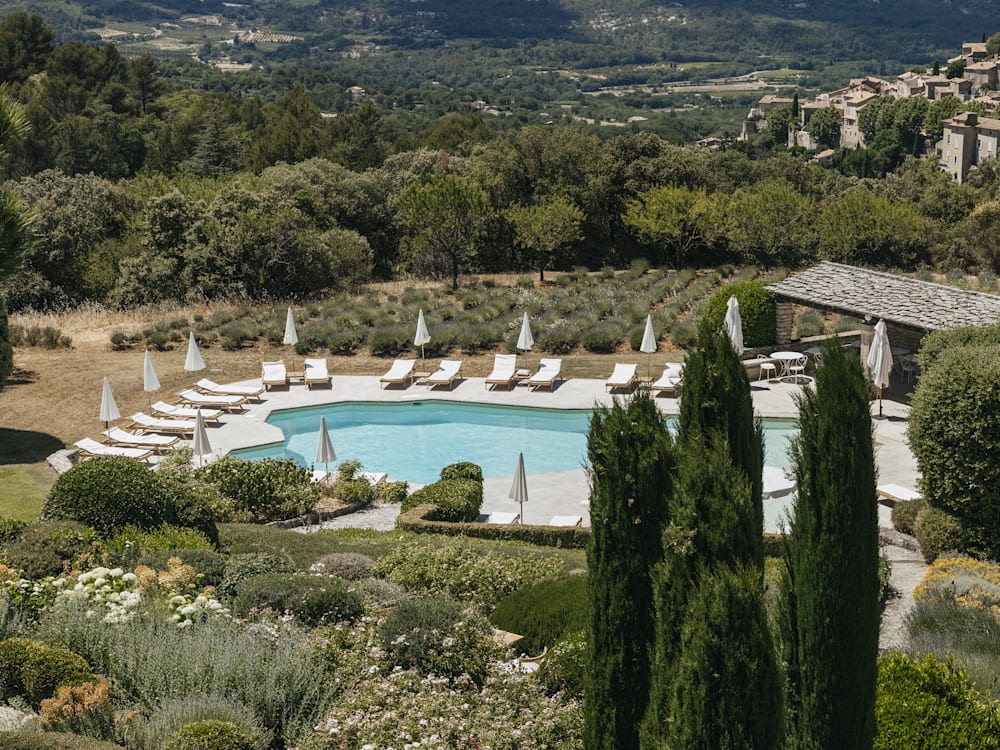 Peeking through the trees lies the swimming pool surrounded by sun loungers above the rolling hills of the valley beyond. 