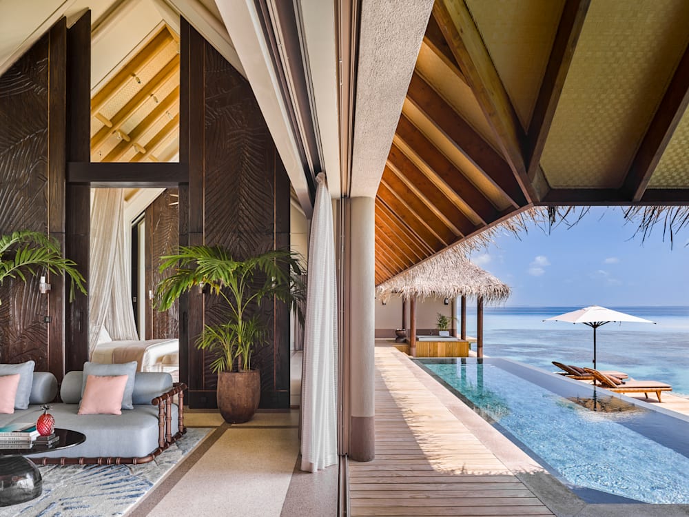 Sideview of an overwater villa, the luxury lounge and high ceilinged bedroom is in view, with the terrace and private swimming pool blending into the ocean. 
