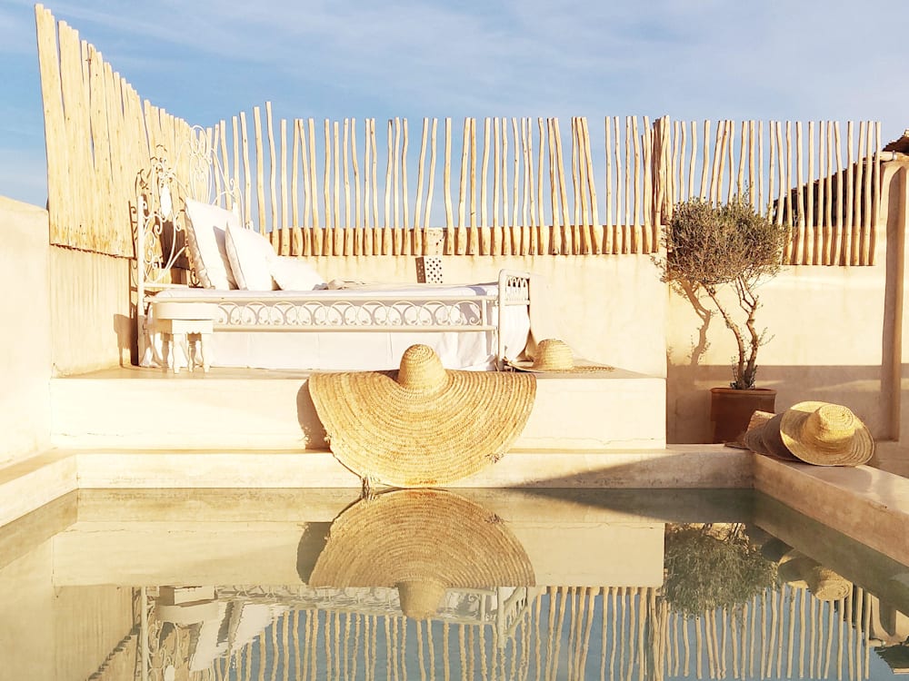 Rooftop swimming pool with sunhat off the side of the pool. The golden afternoon light is highlighting the cream coloured building and creating a mirror like reflection in the surface of the water. 