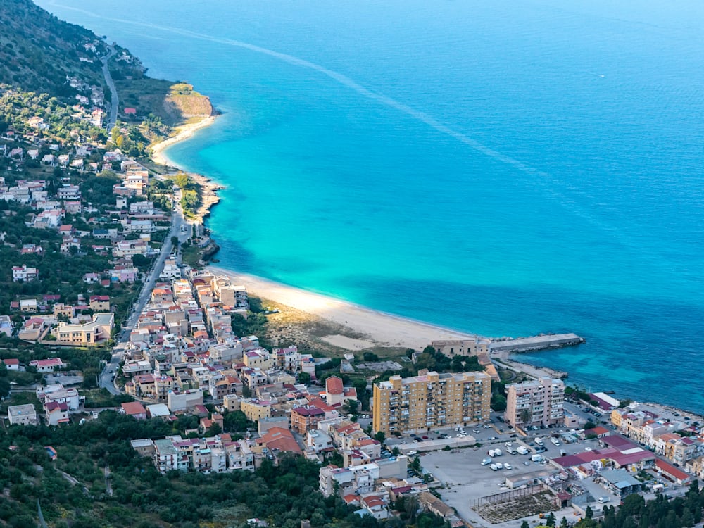 Aerial view of Vergine Maria Beach, the azure blue sea meets sun striken white sands. The white walled, terracotta roof tiled town is in the shadow of the mountains. 