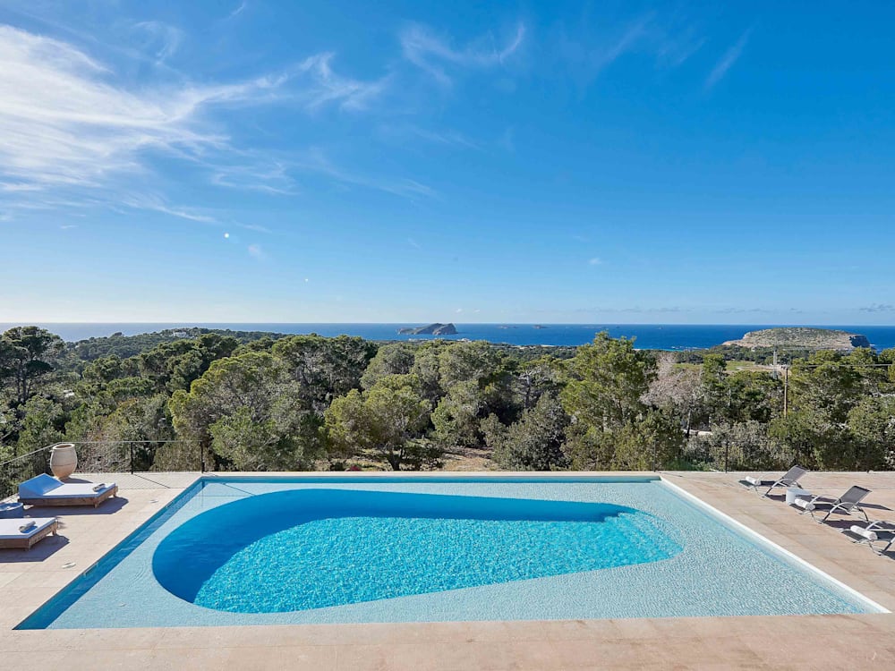 Swimming pool and sun loungers at Sa Serra, Ibiza, underneath a blue sky with views out to the ocean