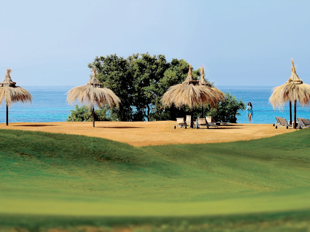 Pantai berpasir dengan kursi berjemur dan payung dari lapangan golf